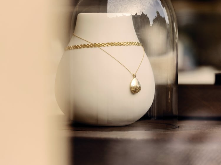 A large, fabric bust sits on a unit, a woven necklace and an engraved gold locket hang.
